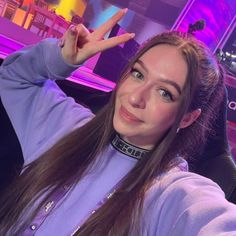 a woman sitting in a chair making the peace sign with her hand while wearing a purple shirt