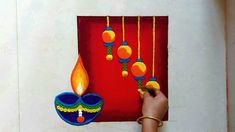 a hand holding a lit candle in front of a painting on a red wall with balls hanging from it