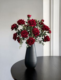 a black vase filled with red roses on top of a table