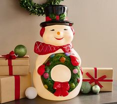 a lighted snowman with a wreath and presents on the table next to it is an ornament