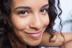 a close up of a person with curly hair and a nose piercing on her cheek