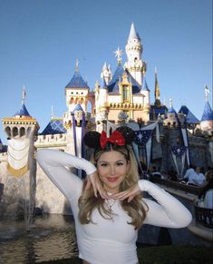 a woman posing in front of a castle with a minnie mouse ears on her head