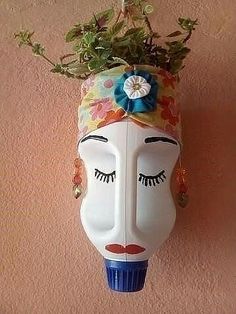 a white mask with flowers on it hanging from the wall next to a potted plant