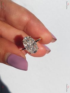 a woman's hand holding a ring with an oval shaped diamond on top of it