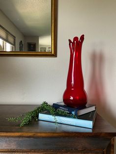 a red vase sitting on top of a wooden table next to books and a mirror