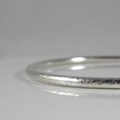 "This handmade heirloom quality sterling silver bangle is such a classic! Made from 3.2mm wide solid round sterling silver, it has such a pleasing weight. It is hand-formed and forged by me... the silver then gets hammered, hammered and hammered some more, creating a surface fully covered in tiny facets that provide a perfectly understated sparkle. The silver has been lovingly sanded and given a polished finish. Available in smooth (unhammered) finish as well, as can be seen in the last two pics Stackable Sterling Silver Bracelet For Anniversary, Stackable Sterling Silver White Gold Bangle, Stackable Sterling Silver Bangle In White Gold, Stackable White Gold Sterling Silver Bangle, Silver Bangle With Sterling Silver Clasp, Sterling Silver Stackable Bangle For Anniversary, Stackable White Gold Sterling Silver Bracelet As Gift, Gift Stackable Sterling Silver Bracelet In White Gold, Minimalist Hammered Sterling Silver Bangle