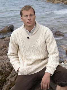 This mans shawl collar cable knit sweater is knit using traditional knitting patterns from Ireland. The “V” neck shawl collar is the main feature of this Irish sweater. It is completed with the use of an old-style button closure. The diamond knitting pattern along the body is said to represent wealth and success. The traditional cable pattern symbolizing fisherman’s ropes unite the past with the modern-day. The use of the herringbone stitch along the body and the length of the arms is further li Diamond Knitting Pattern, Irish Wool Sweaters, Irish Knitwear, Irish Sweater, Irish Style, Shawl Collar Sweater, Herringbone Stitch, Aran Sweater, Fisherman Sweater