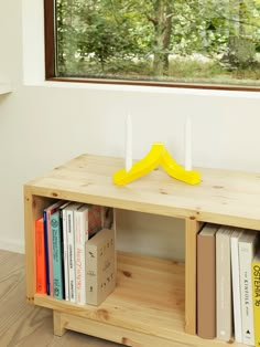 a wooden shelf with two candles on top of it and books in front of the window