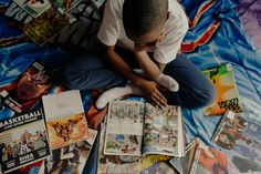 a man sitting on top of a bed covered in comics and magazines, with his head resting on his hand