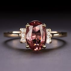 an oval shaped pink tourmaline surrounded by three smaller white diamonds on a yellow gold band