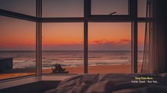 a bed sitting in front of a window next to the ocean at sunset or dawn