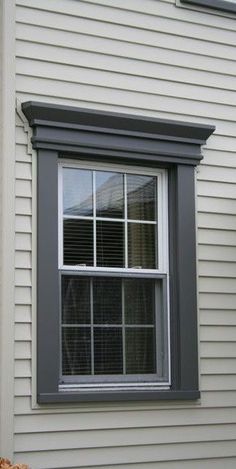 a white house with grey trim and window on the outside wall, in front of it is a planter filled with flowers