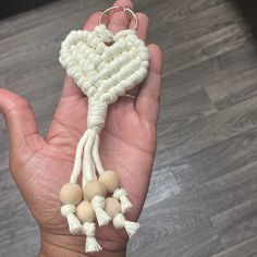 a hand holding a white heart shaped keychain with tassels on it