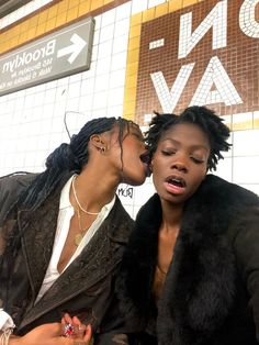 two women are kissing each other in front of a subway station sign that says don't leave