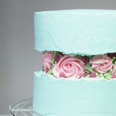 there is a blue cake with pink flowers on the top and bottom layer, decorated with green icing