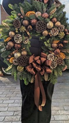 a man is holding a wreath with pine cones and other decorations