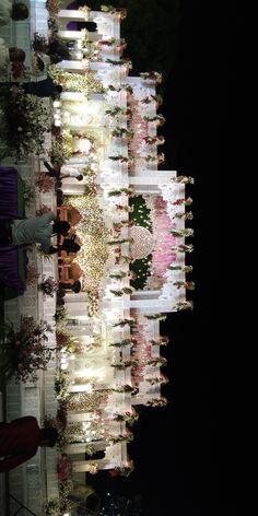 people are standing in front of a building with flowers on the side and lights reflecting off it