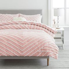 a bed with pink comforter and pillows in a room next to a white wall