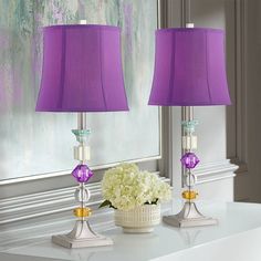 two purple lamps sitting on top of a table next to a vase with white flowers