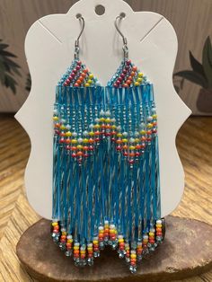 a pair of blue earrings with multicolored beads on top of a piece of wood