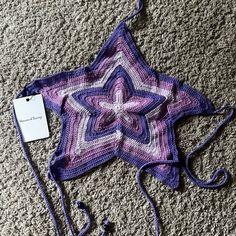 a purple crocheted star is laying on the floor next to a white tag