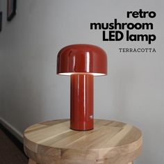 a red lamp sitting on top of a wooden table next to a white wall with the words retro mushroom led lamp above it