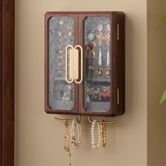 a wooden wall mounted jewelry holder with glass doors and gold hardware hanging from it's sides