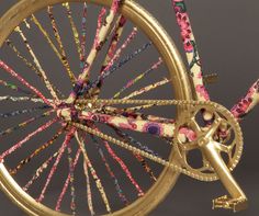 a gold bicycle with pink and blue flowers on it's spokes is shown against a gray background