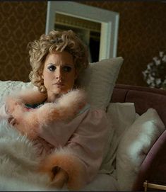 a woman laying on top of a bed covered in fluffy white blankets and holding a teddy bear