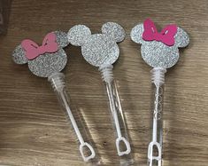 three mickey mouse shaped toothbrushes with pink and silver bows on them, sitting next to each other