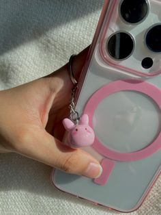 a person holding a pink phone case with a pig keychain attached to it