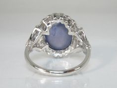 We love this Art Deco era star sapphire ring featuring a gorgeous oval cabochon blue star sapphire weighing 6.71 carats. The ring is crafted in 5.6 grams of platinum and is absolutely stunning in it style and materials. Total diamond weight is an estimated 0.44 carats, with two straight baguette diamonds weighing an estimated 0.10 carats combined and 26 rounds single cut diamonds weighing an estimated 0.34 carats combined. The stones are lovely accents to the star sapphire and are super fiery, g Formal Oval Cabochon Sapphire Ring, Collectible Oval Cabochon Moonstone Ring, Vintage Oval Cabochon Sapphire Ring For Formal Occasions, Silver Cabochons For Formal Fine Jewelry, Elegant Blue Oval Cabochon Moonstone Ring, Fine Jewelry Silver Cabochons For Formal Occasions, Silver Cabochons For Formal Occasions, Heirloom Oval Cabochon Sapphire Ring, Antique Cabochon Sapphire Ring For Formal Events