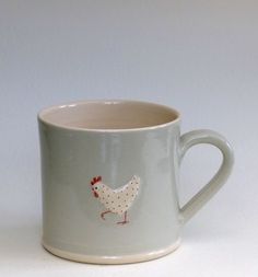 a coffee cup with a rooster painted on the side, sitting in front of a white background