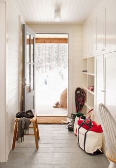 a hallway with white walls and flooring next to a wooden bench in front of an open door