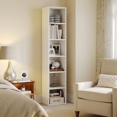 a white book shelf in a bedroom next to a chair and lamp on a table