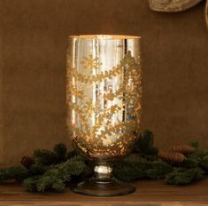 a lit candle is sitting on a table with pine cones and evergreen branches around it