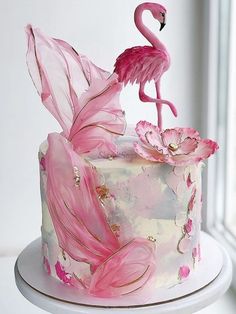 a pink flamingo cake sitting on top of a white table next to a window