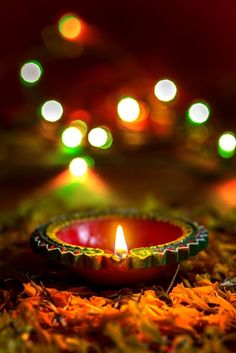 a lit candle sitting on the ground with lights in the background