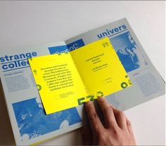 a person holding an open book with yellow paper on the pages and blue text reading strange college