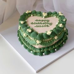 a heart - shaped cake with green icing and white flowers on the top is sitting on a table