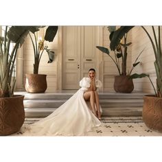 a woman in a white dress sitting on the ground next to some potted plants