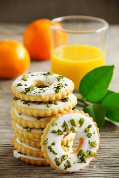 a stack of cookies with white frosting and sprinkles next to orange juice