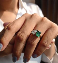 a woman's hand holding an emerald and diamond ring