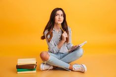 a young woman sitting on the floor holding a book and looking up at something in front of her