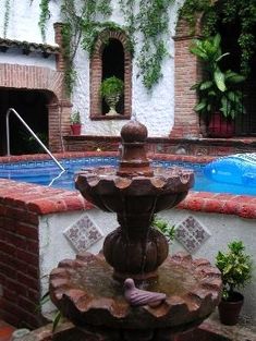 a fountain in the middle of a courtyard with a swimming pool and brick walls around it