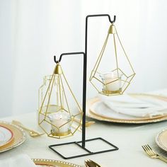 the table is set with gold plates, silverware and glass vases in geometric shapes