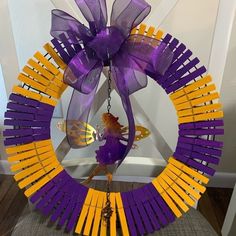 a purple and yellow wreath with a fairy on it, hanging from a chain in front of a white wall