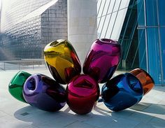 several colorful vases sitting on the ground in front of a tall building with glass windows