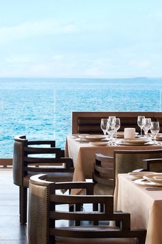 an outdoor dining area overlooking the ocean with tables and chairs set up for two people