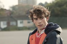 a young man with curly hair wearing an orange and black jacket looking at the camera